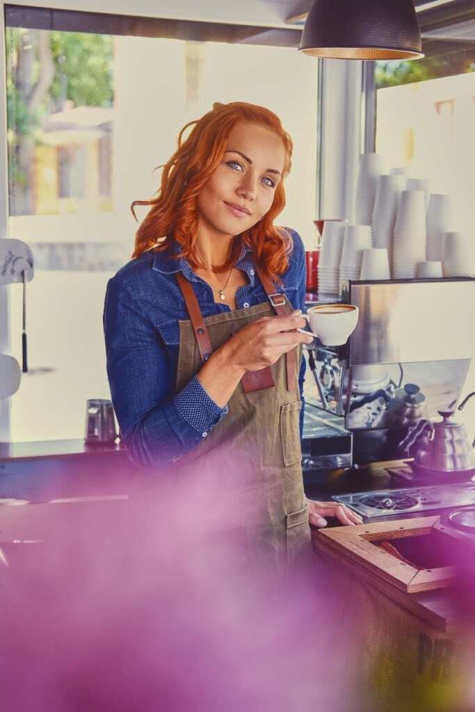 Eine junge Frau mit roten Haaren und einem Kaffee in der Hand - dank ihrer Webpräsenz von opticore solutions finden ihre Kunden sie genau dort, wo sie sie brauchen